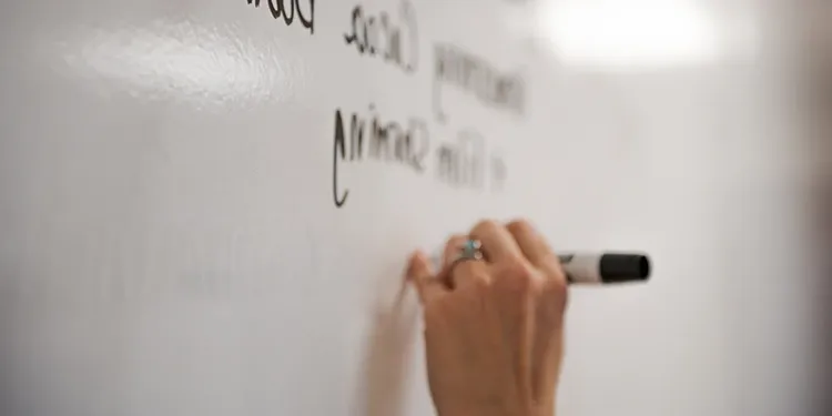 A close up of a hand writing on a white board